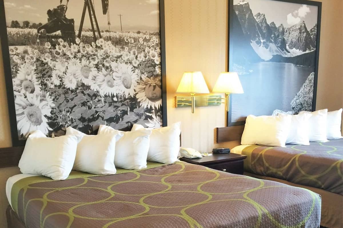 Ein Hotelzimmer mit zwei Betten, einem Nachttisch, Lampen und zwei großen, gerahmten Bildern an den Wänden.