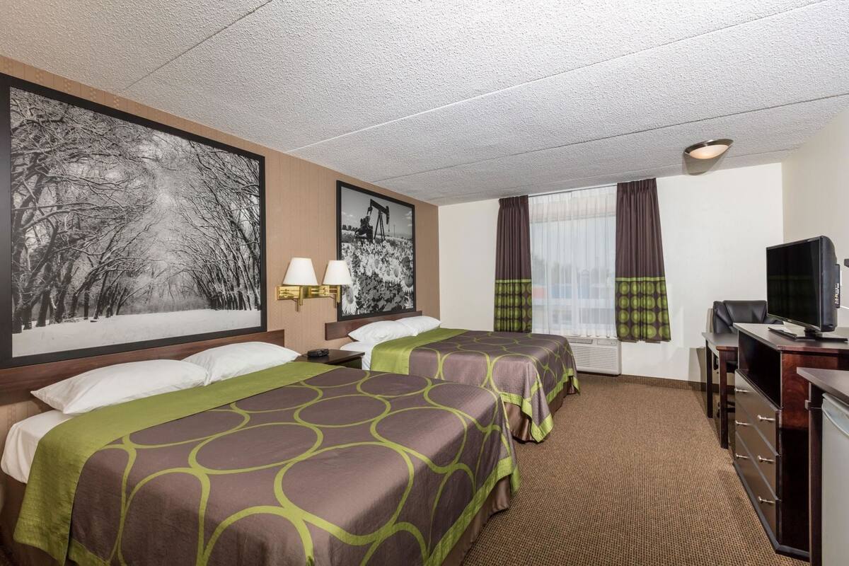 Ein Hotelzimmer mit zwei Betten, einem Schreibtisch mit Computer, einem Fernseher und großen, gerahmten Bildern an der Wand.