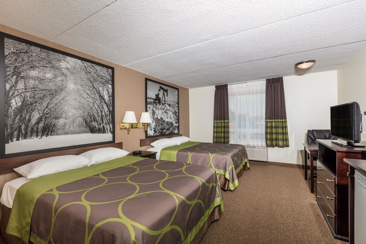 Ein Hotelzimmer mit zwei Betten, einem Schreibtisch mit Fernseher und einem großen Bild in einem Rahmen an der Wand.