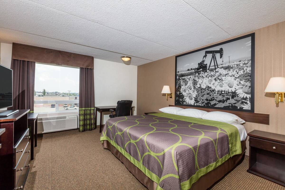 Ein Hotelzimmer mit einem großen Bett, einem Schreibtisch, einem Stuhl, einem Fernseher und einem Fenster mit Vorhängen.