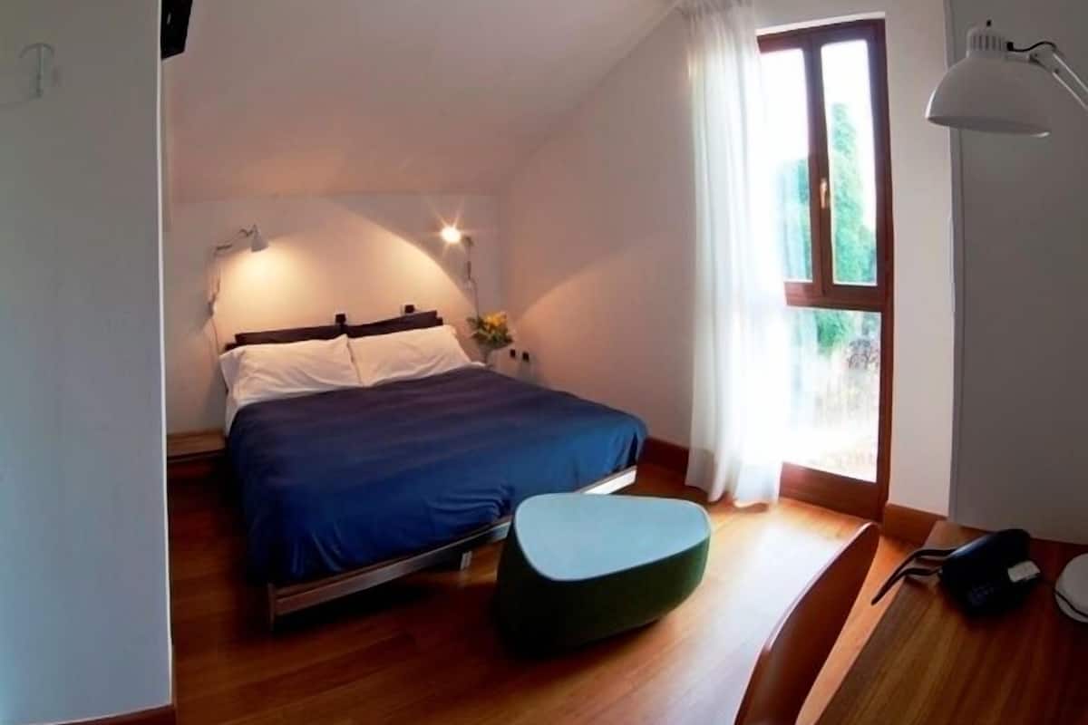 A bedroom with a bed, a bedside table, a lamp, and a window with curtains.