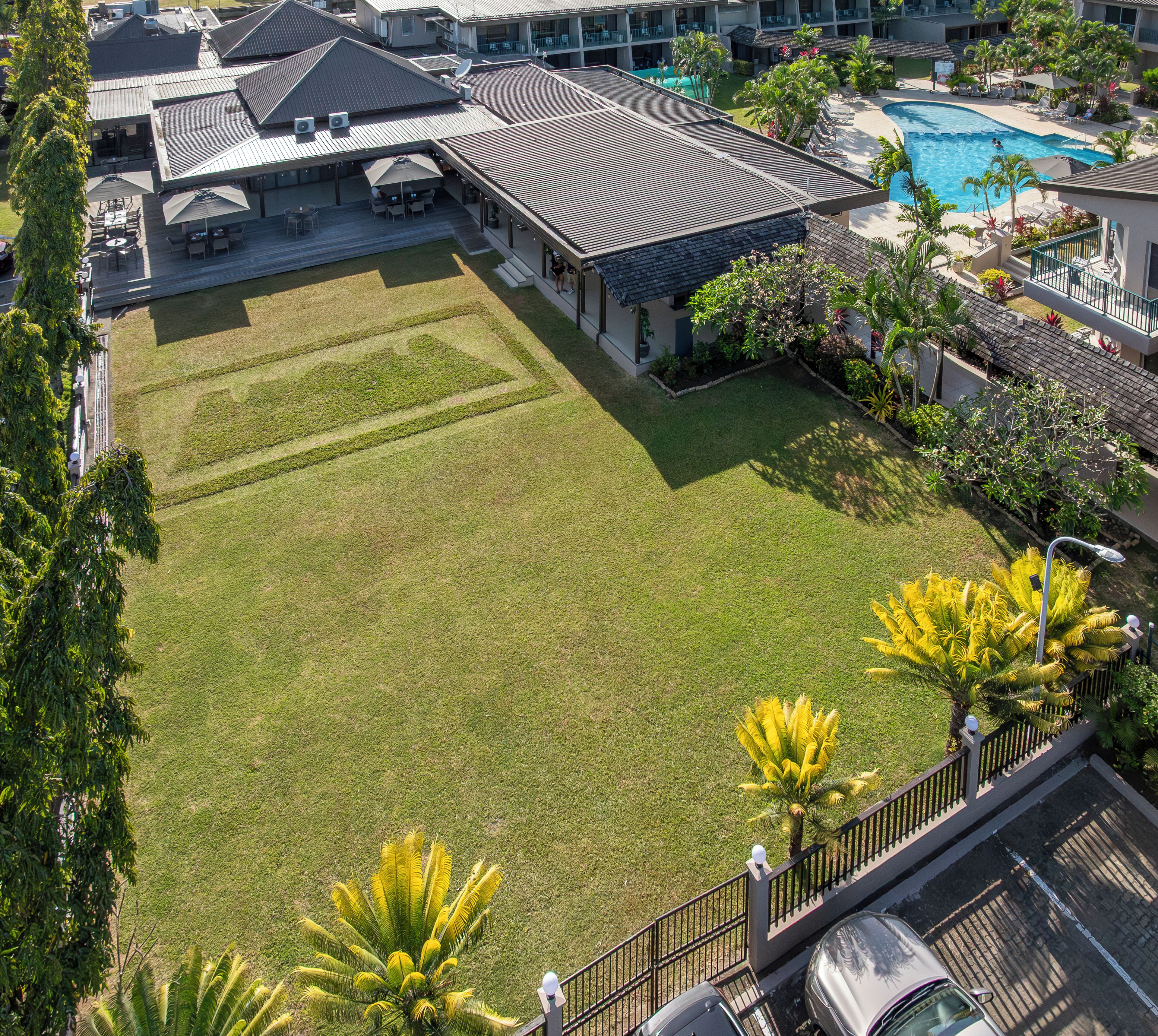 A hotel with a swimming pool, a covered patio, and a well-maintained lawn.