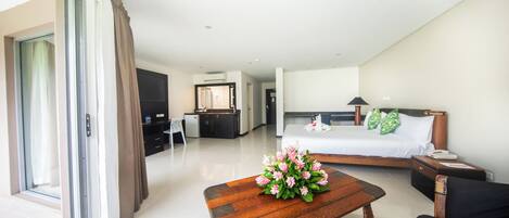 Una habitación de hotel moderna con una cama, una mesa de centro de madera con flores, un sofá negro, un escritorio y un televisor.