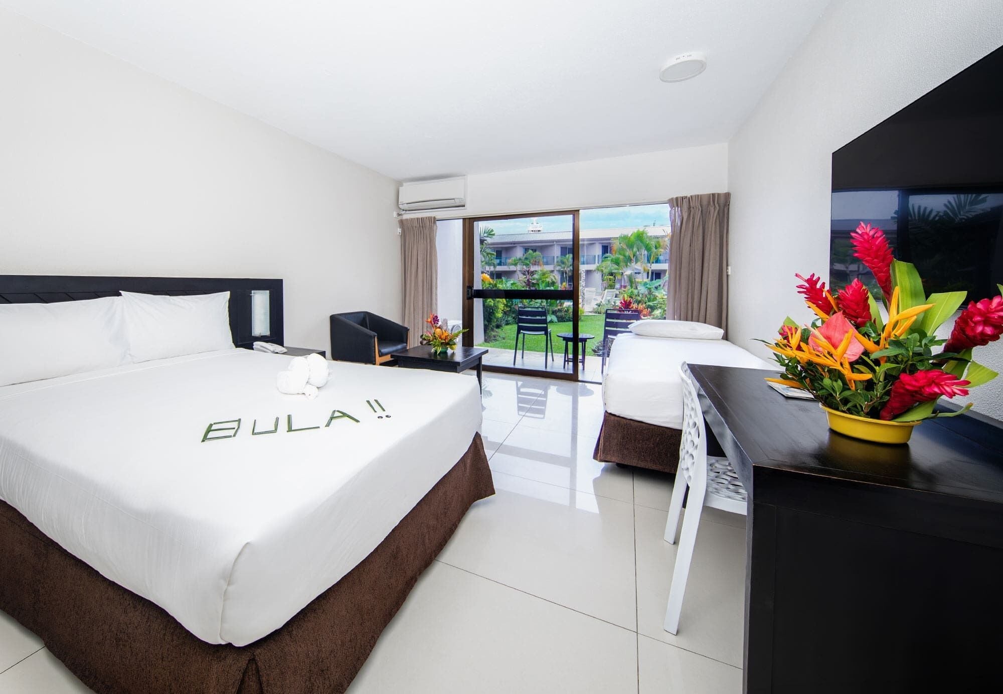 Habitación de hotel con cama, escritorio, silla y vistas a un edificio y vegetación.
