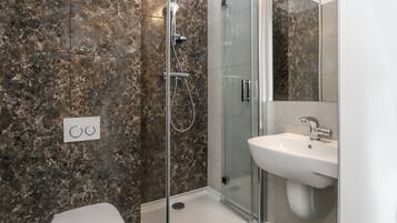 A modern bathroom with a glass-enclosed shower, a white sink, and a toilet.