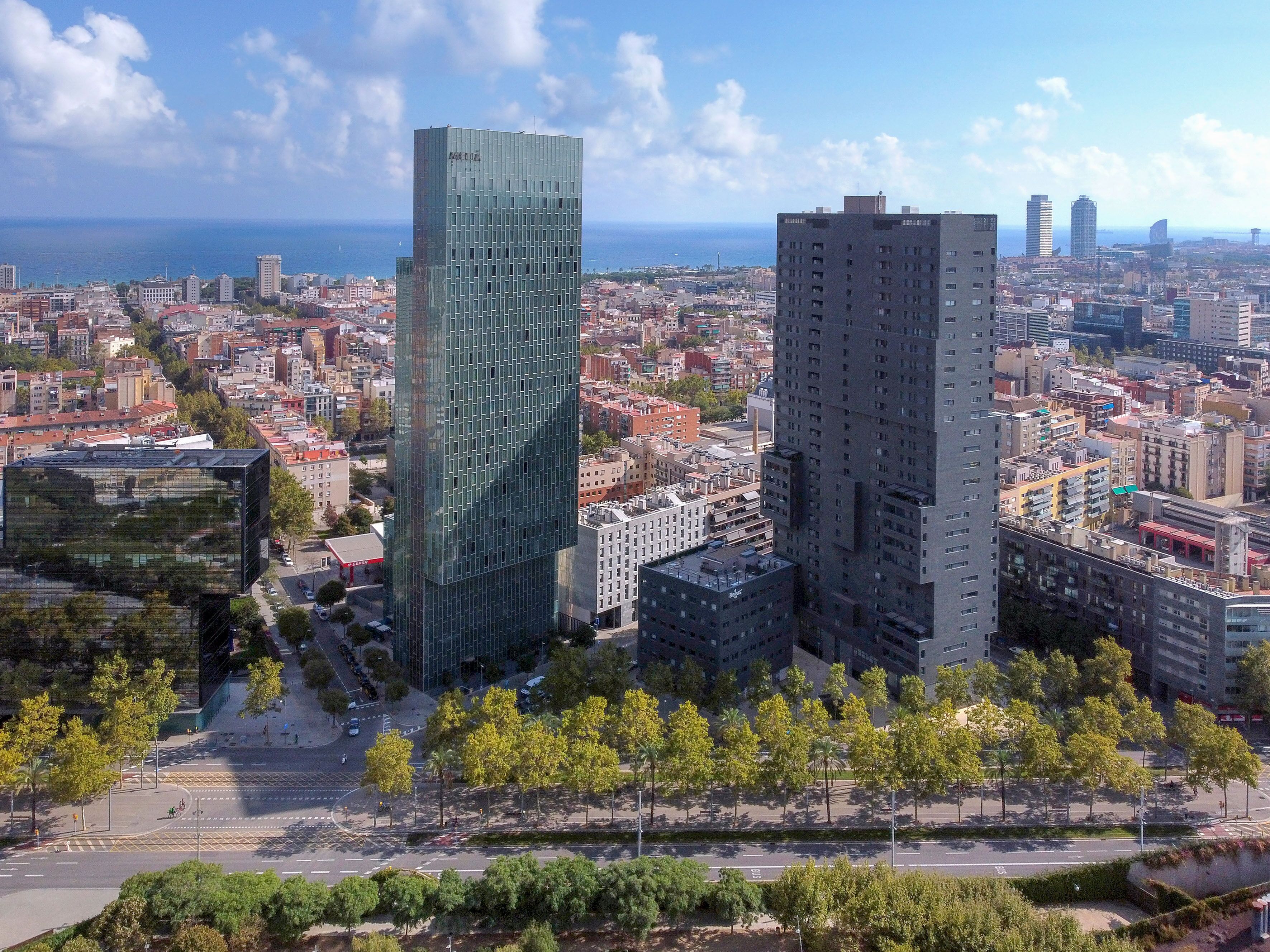 A cityscape with modern high-rise buildings, a clear sky, and a distant view of the sea.