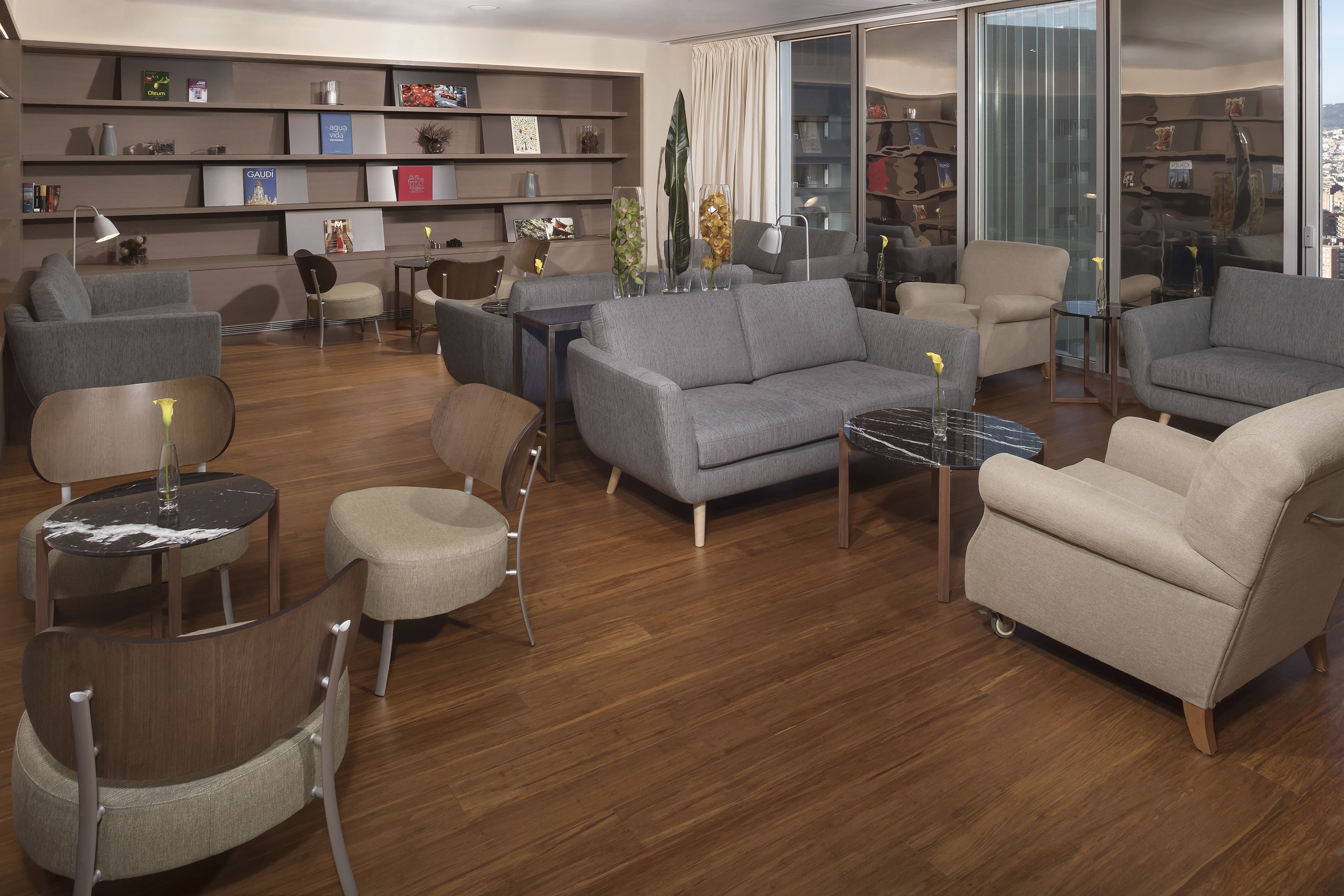 Una sala de estar moderna con un sofá gris, sillones, una mesa de centro y una estantería llena de objetos decorativos.