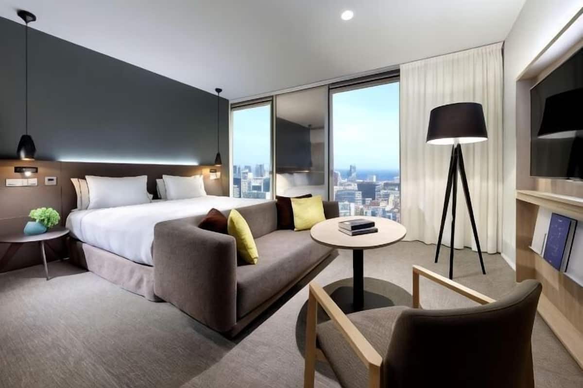 Quarto de hotel moderno com cama, sofá, poltrona e uma pequena mesa.