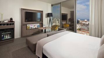 Habitación de hotel con una cama grande, televisión, escritorio con silla y vista a la ciudad desde la ventana.