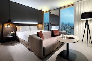 A modern hotel room with a large bed, a sofa, a small table, and a city view. - Melia Barcelona Sky (Barcelona)