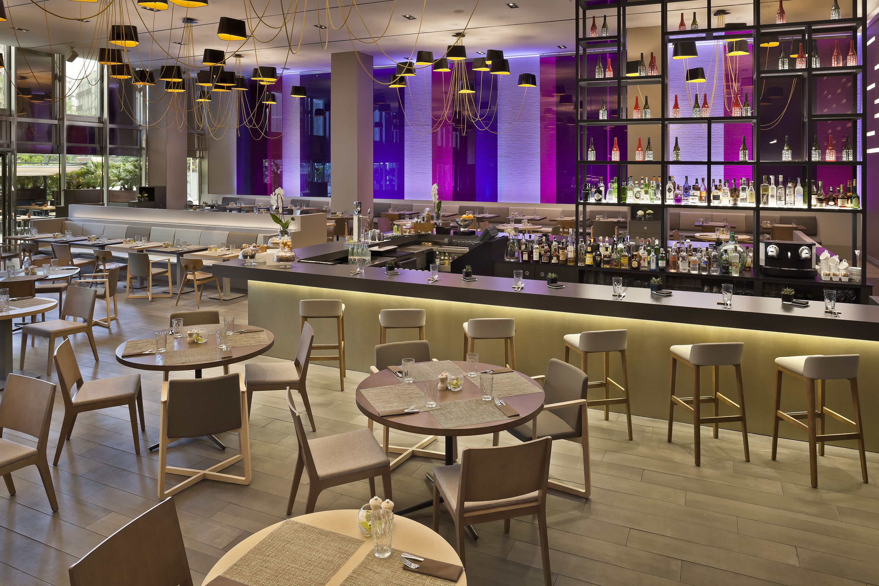 A modern bar area with round tables and bar stools, a well-stocked liquor cabinet, and a view of the outdoor seating area.
