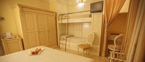Habitación de hotel con literas, un escritorio con silla, un televisor y una pequeña mesa con fruta.