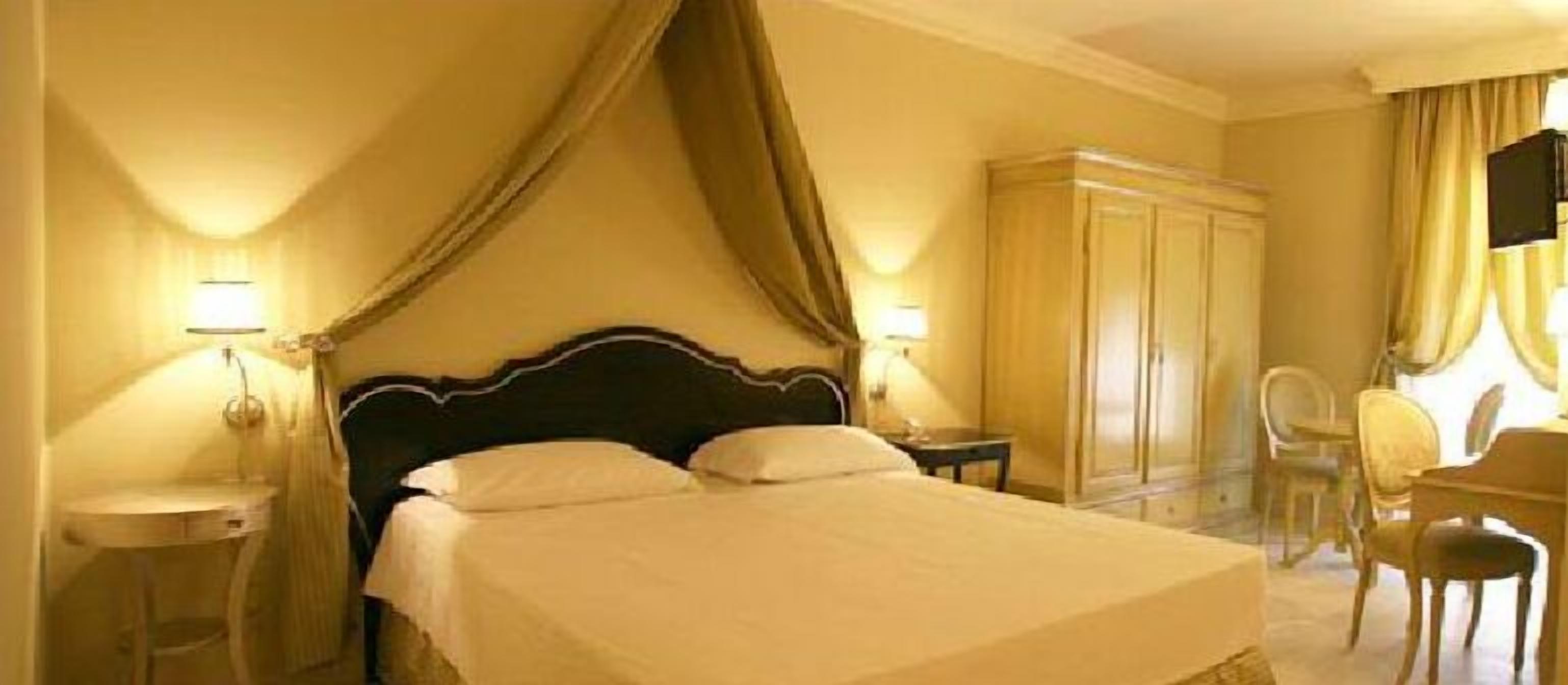 A hotel room with a large bed, a wardrobe, a desk, and a chair.
