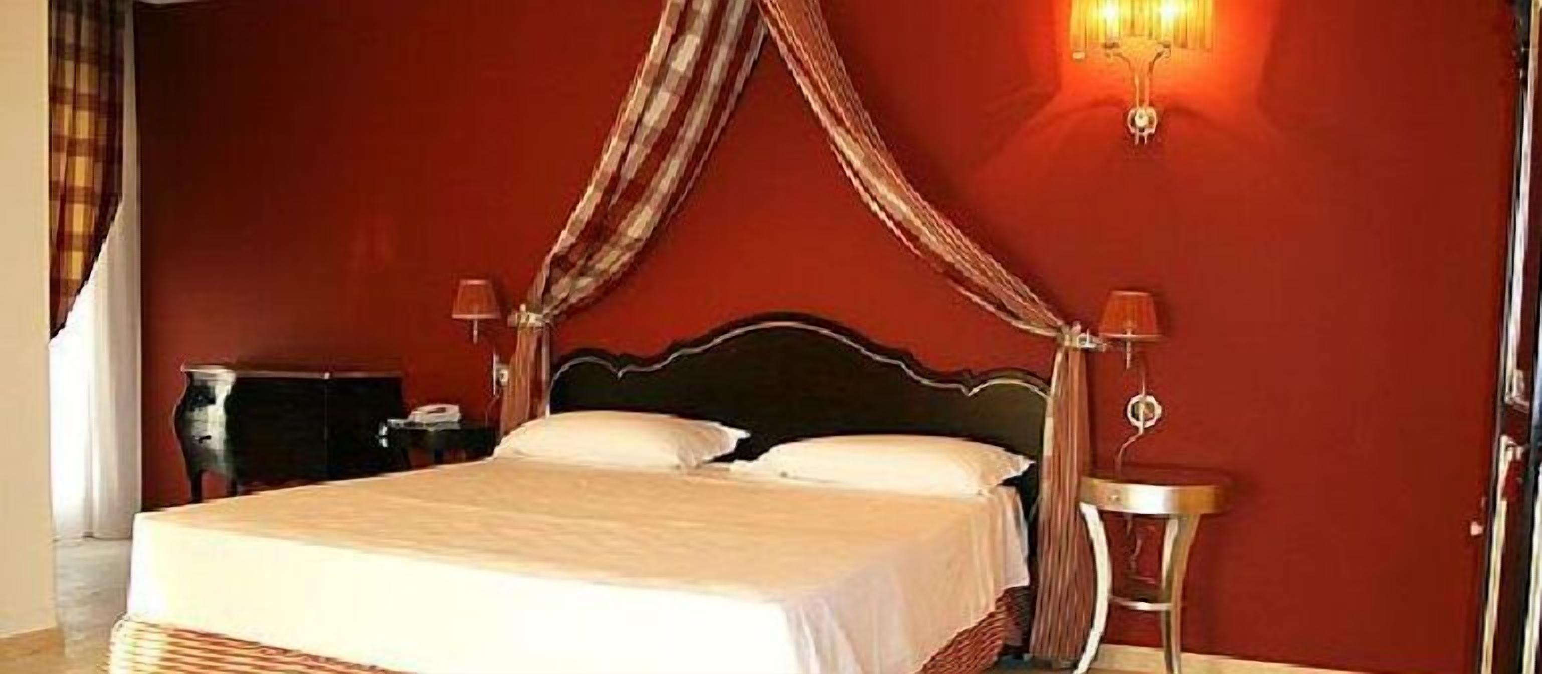 A hotel room with a large bed, a nightstand, a lamp, and a wall-mounted light fixture.