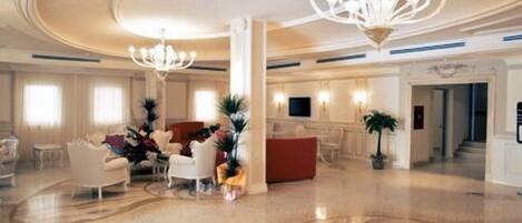 A spacious lobby with a grand chandelier, elegant furniture, and a large decorative rug.
