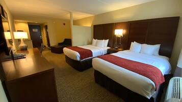 A hotel room with two beds, a desk, a chair, and a lamp.