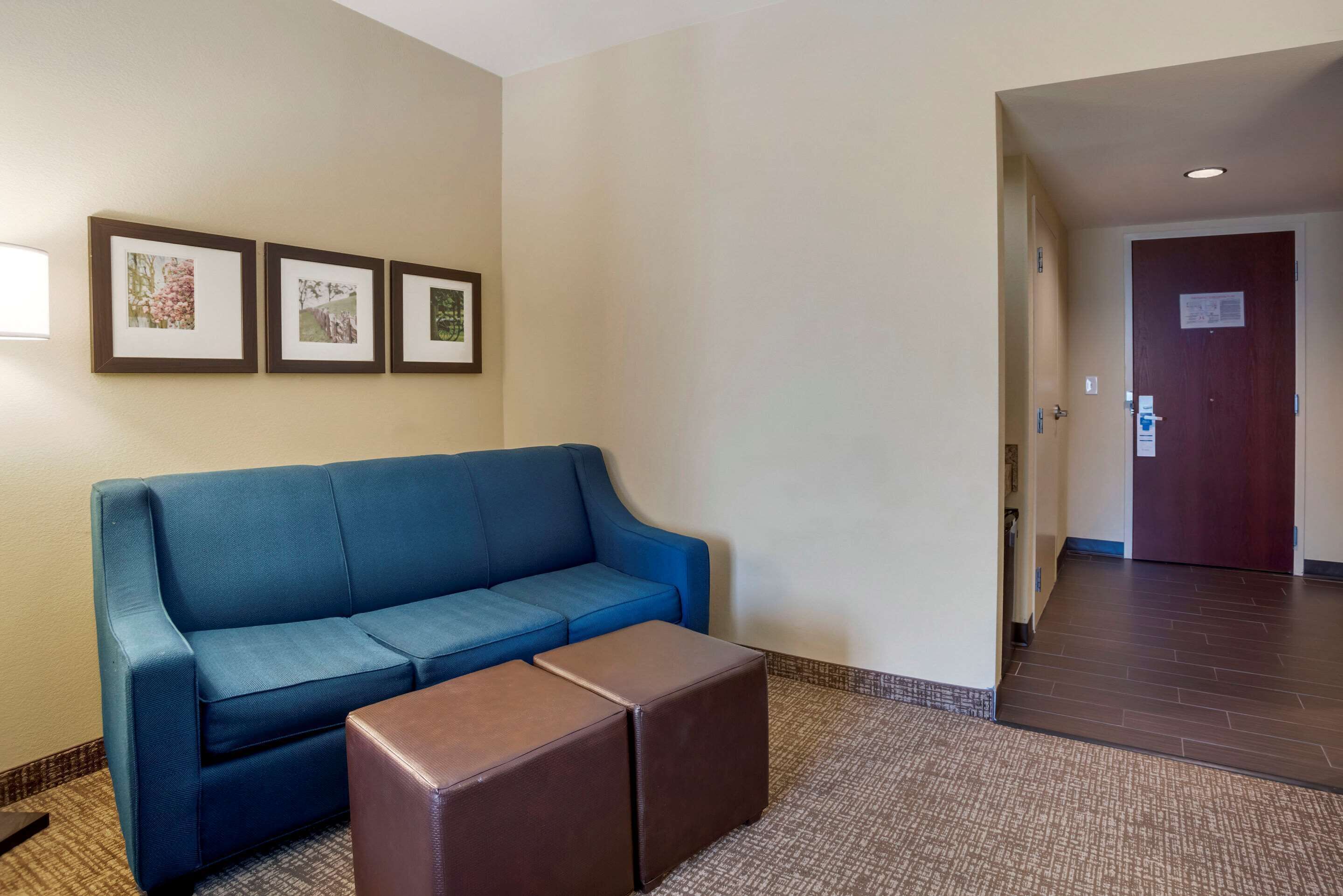 Un vestíbulo de hotel con un sofá azul, un reposapiés marrón y tres cuadros en la pared.