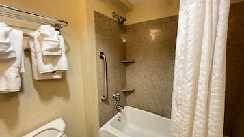 Et badeværelse med toilet, brusebad med gelænder og badekar.