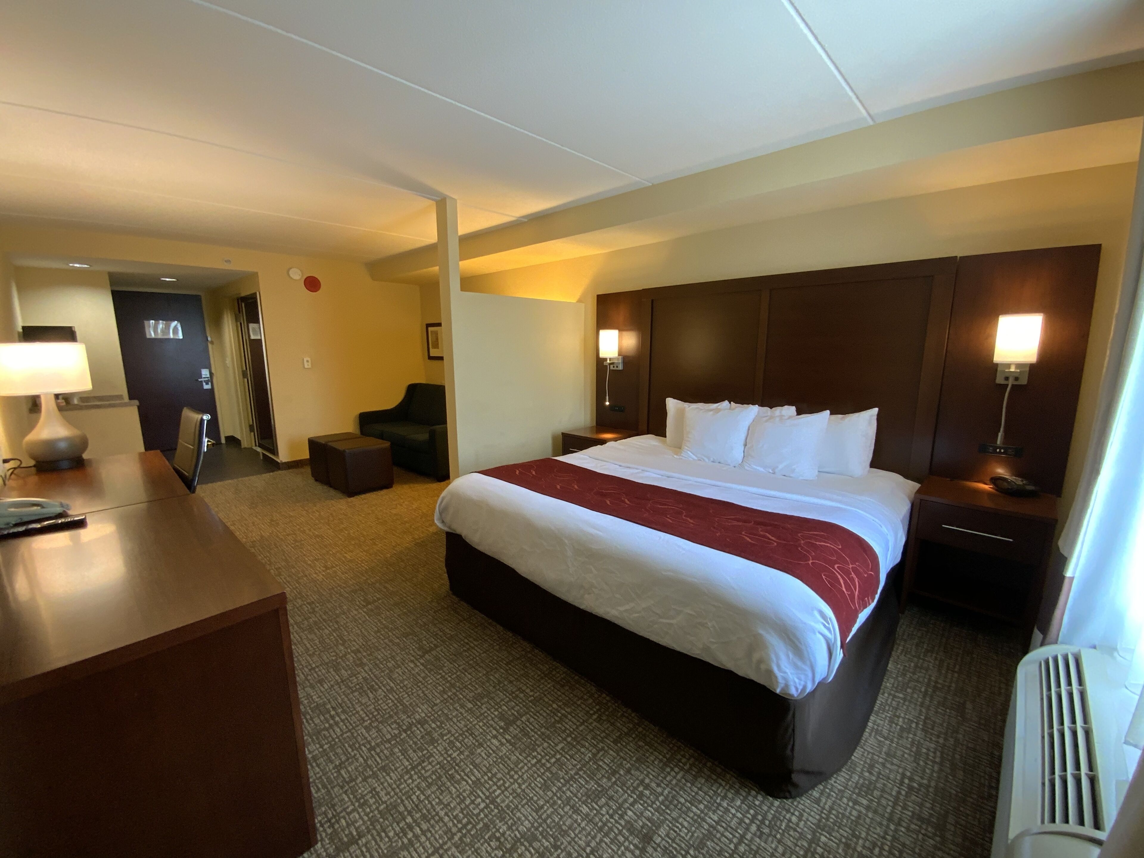 Habitación de hotel con una cama grande, un escritorio con lámpara, una silla y una mesita.