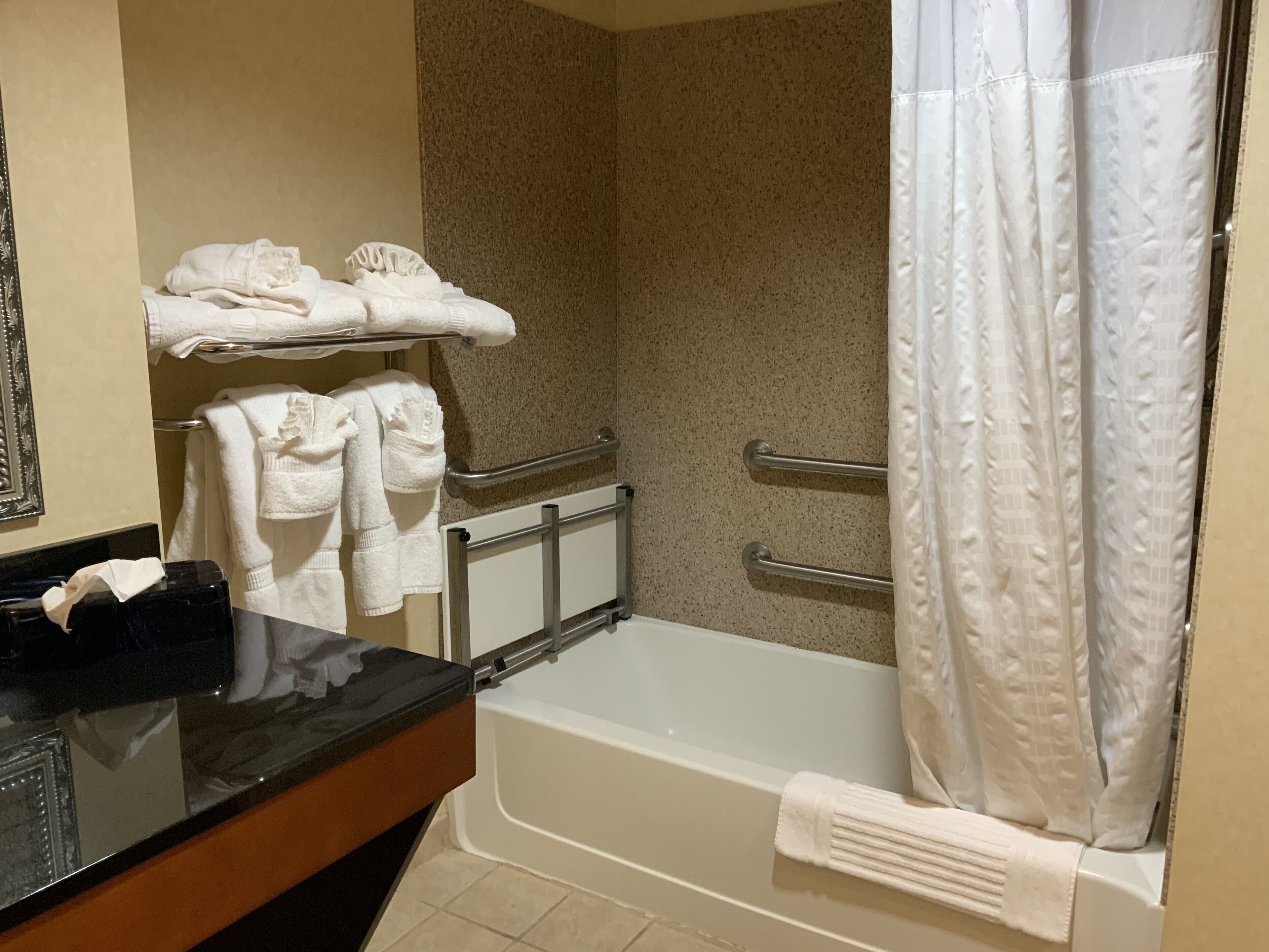A bathroom with a bathtub, a towel rack with folded towels, a handrail, and a shower curtain.