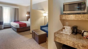 Habitación de hotel con cama, escritorio, microondas, cafetera y ventana con cortinas.