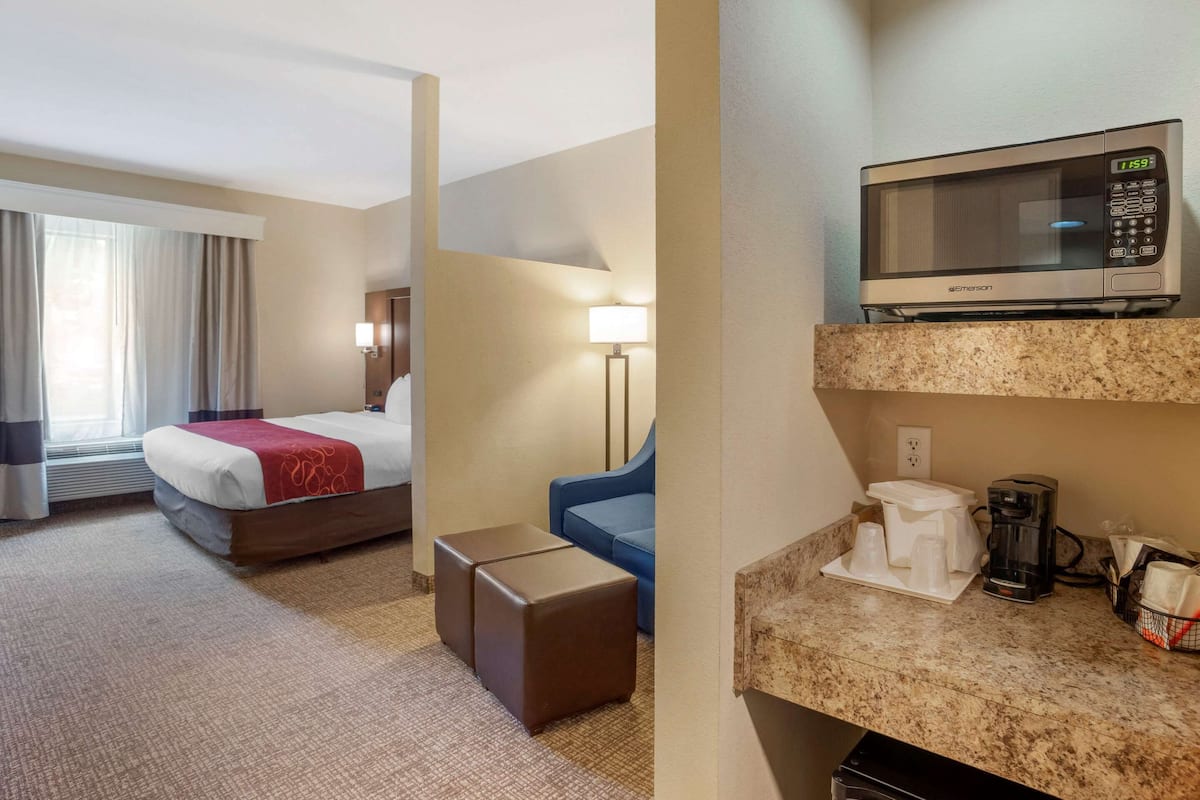 Habitación de hotel con cama, escritorio, microondas, cafetera y ventana con cortinas.