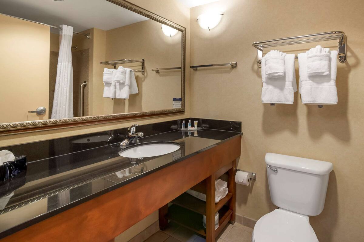 Un baño con lavamanos, espejo, toallero y retrete.