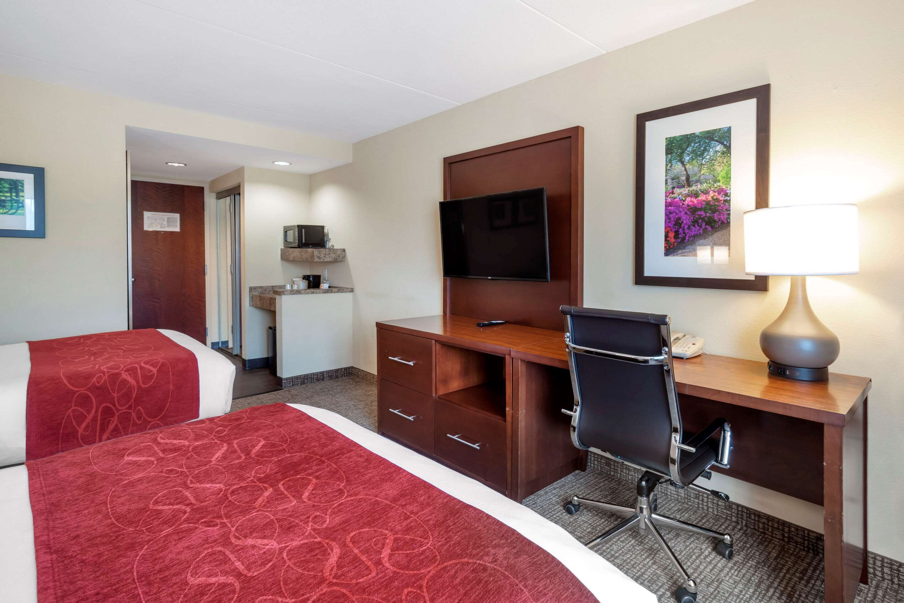 A hotel room with two beds, a desk with a chair, a television, a desk lamp, and a framed picture on the wall.