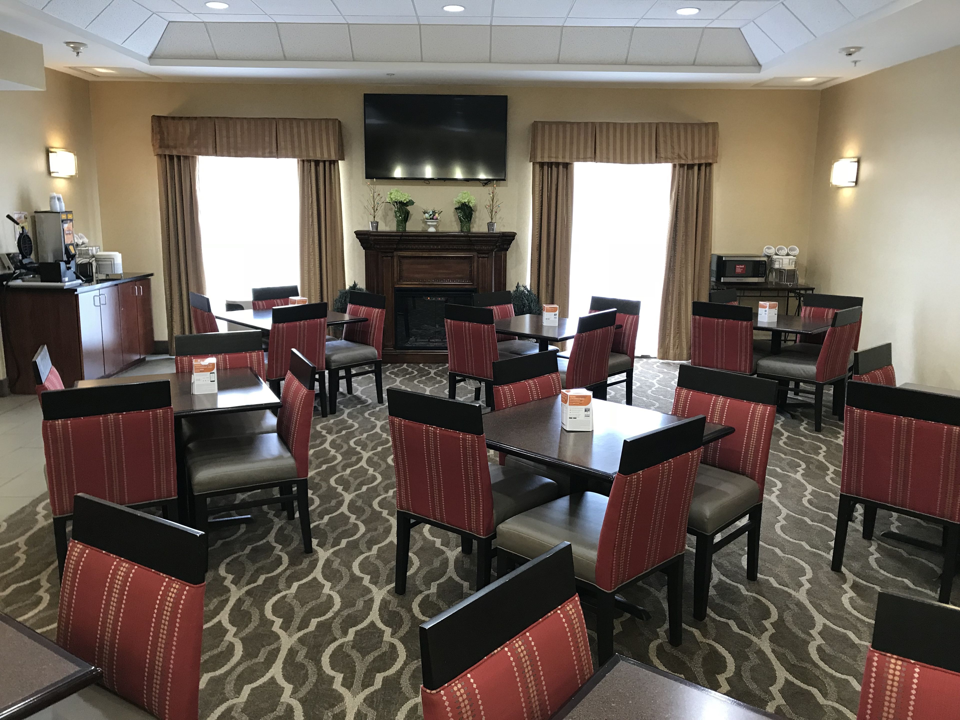 Un espace de restauration d’hôtel comprenant plusieurs tables et chaises, une cheminée et un téléviseur à écran plat fixé au mur.