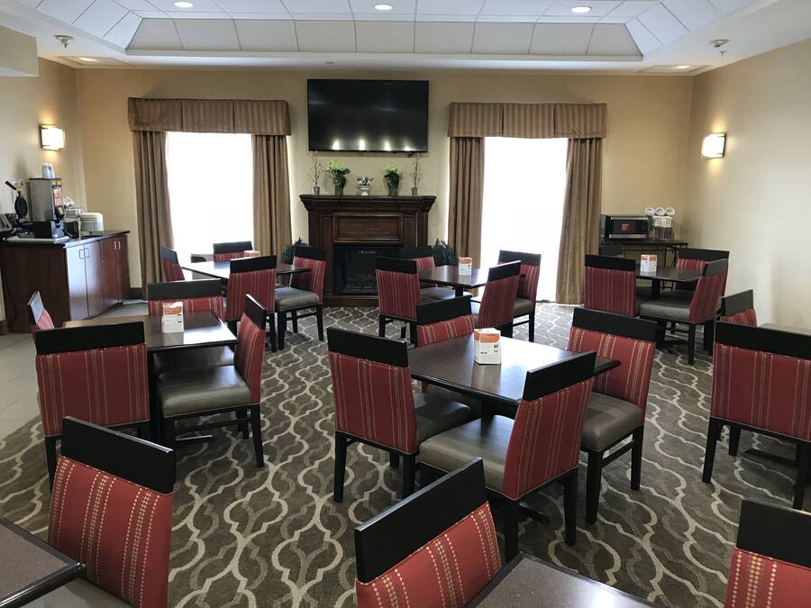A hotel dining area with multiple tables and chairs, a fireplace, and a flat-screen TV mounted on the wall.