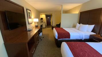 A hotel room with two beds, a desk, a chair, a TV, and a lamp.