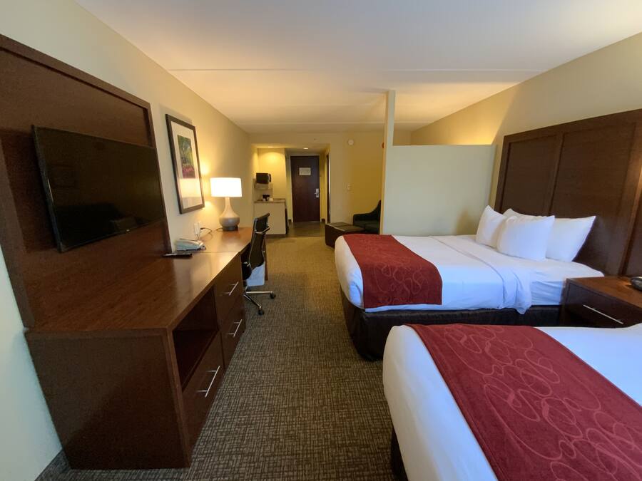 A hotel room with two beds, a desk, a chair, a TV, and a lamp.