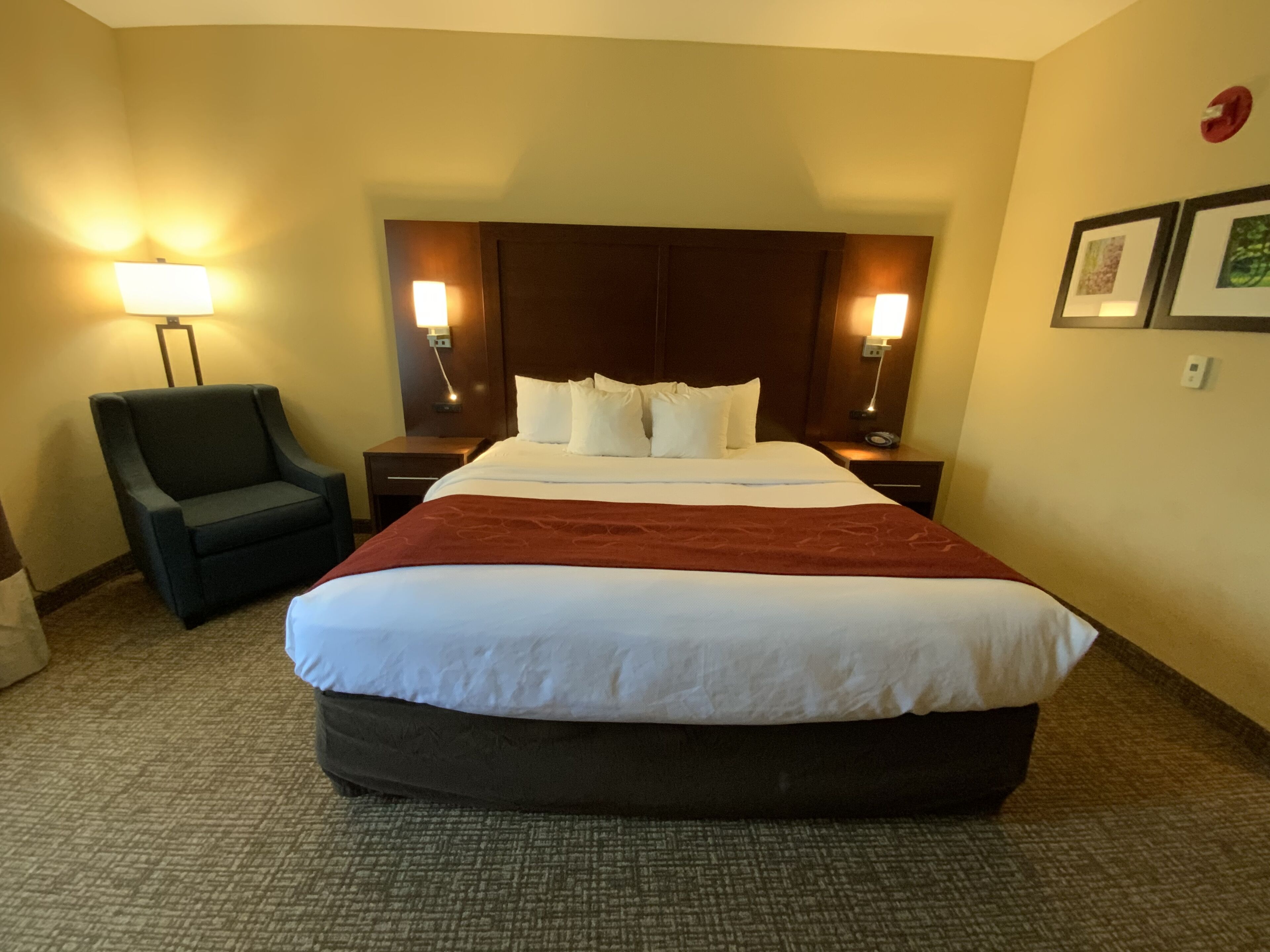 Una habitación de hotel con una cama grande, una silla, mesitas de noche y lámparas fijadas a la pared.