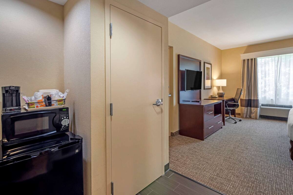Una habitación de hotel con microondas, cafetera, escritorio y silla, y televisor.