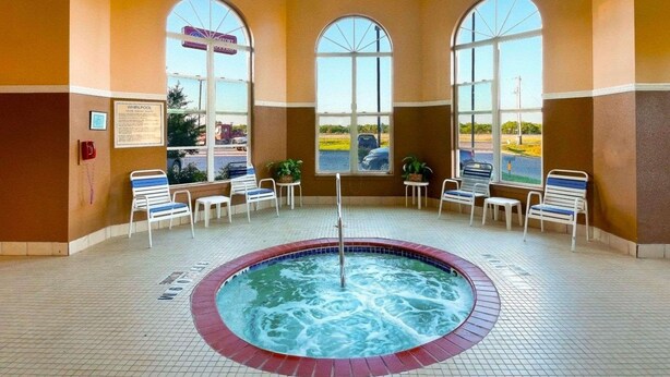 A hot tub area with three arched windows, lounge chairs, and a tiled floor. - Comfort Suites University (Abilene)