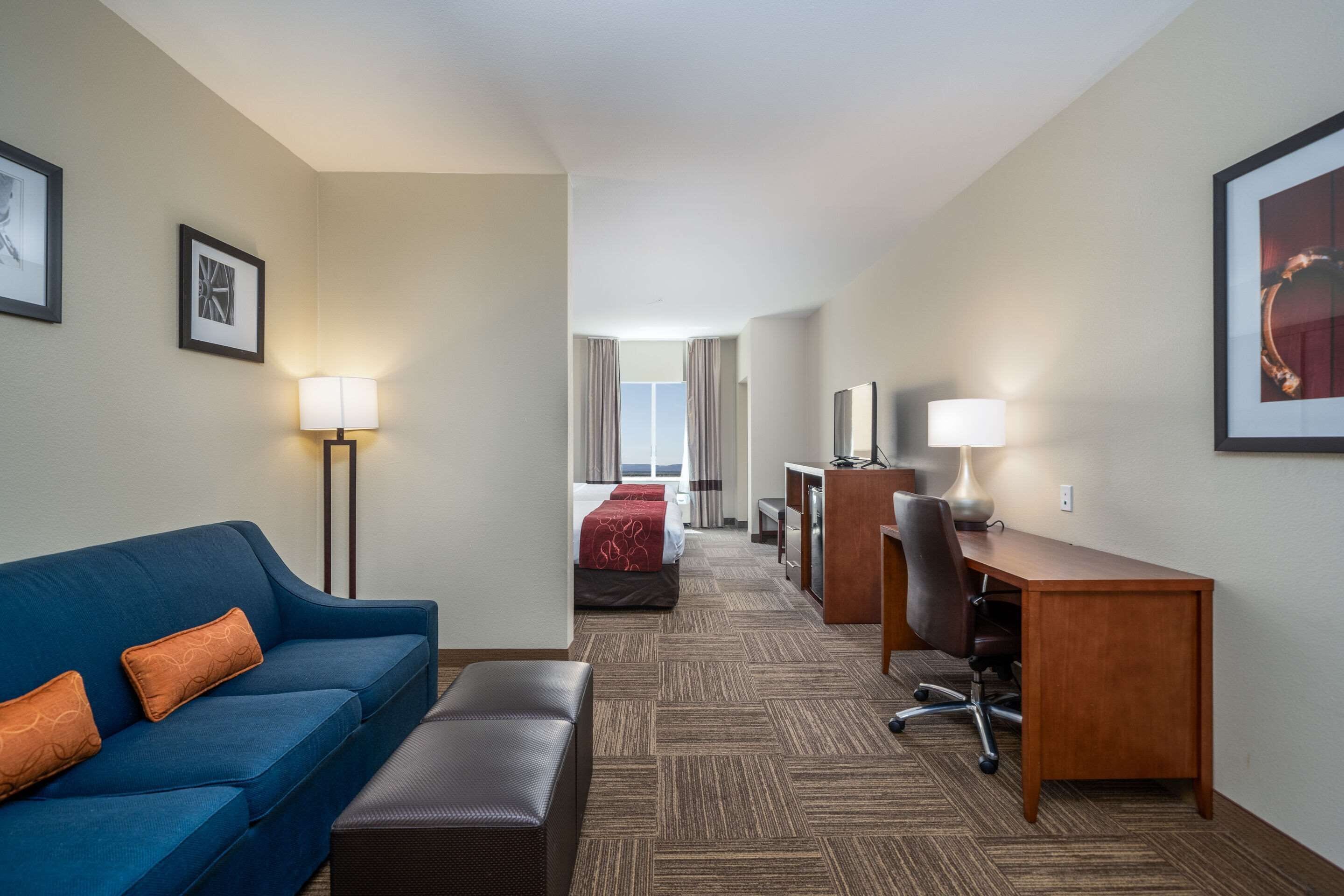 A hotel room with a blue sofa, a wooden desk, a bed with red bedding, and a view of the room's interior.