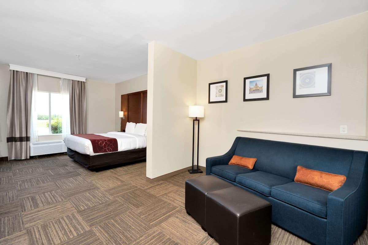 A hotel room with a bed, a blue sofa, a standing lamp, and framed pictures on the wall.