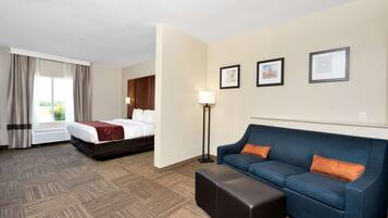 A hotel room with a bed, a blue sofa, a standing lamp, and framed pictures on the wall.