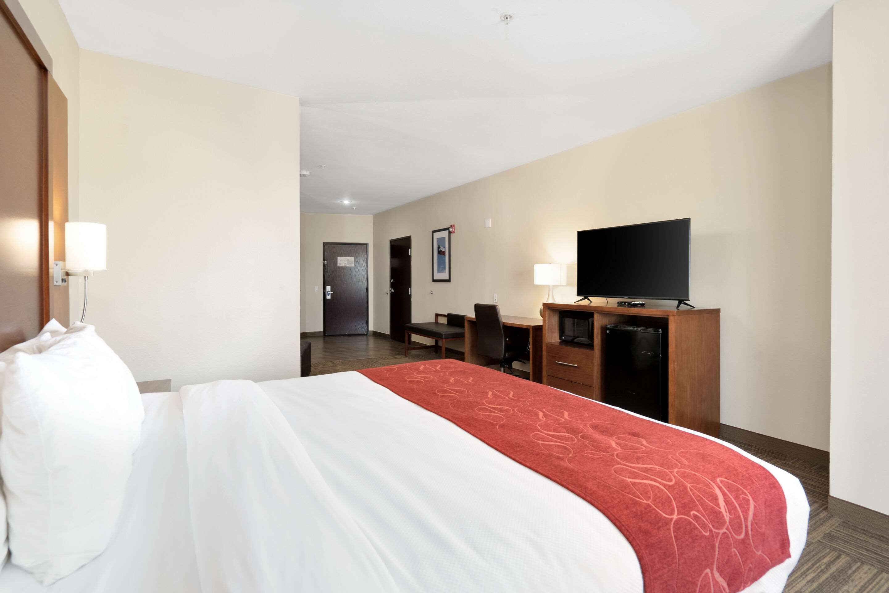 Habitación de hotel con una cama grande, un escritorio con silla, televisión y minibar.