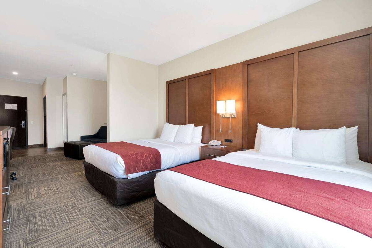 A hotel room with two beds, a wooden headboard, a nightstand, and a desk with a chair.
