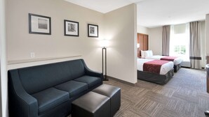A hotel room with a sofa, a standing lamp, and two beds with red bedding. - Comfort Suites University (Abilene)