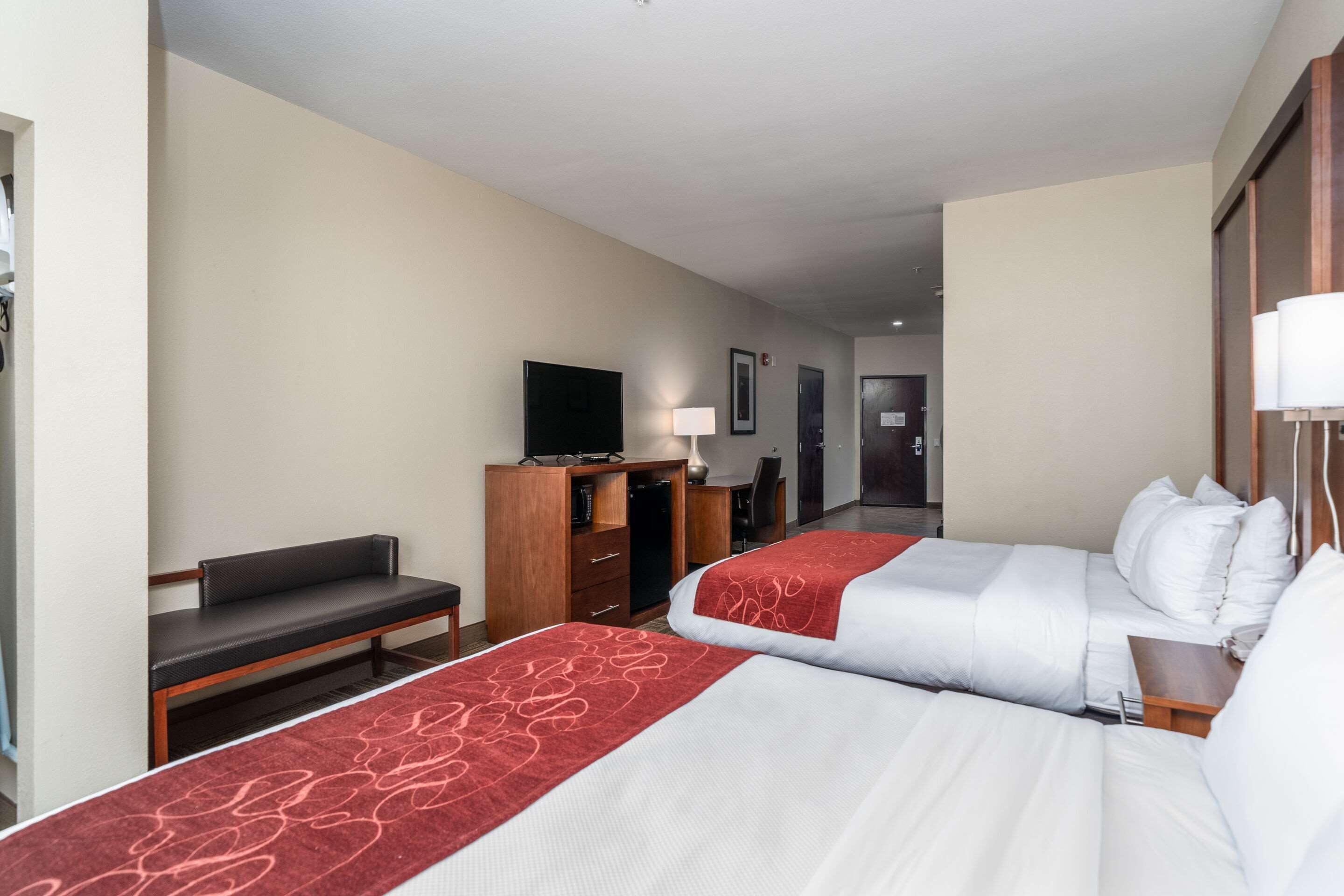 Habitación de hotel con dos camas, un escritorio, una silla, un televisor y un armario.