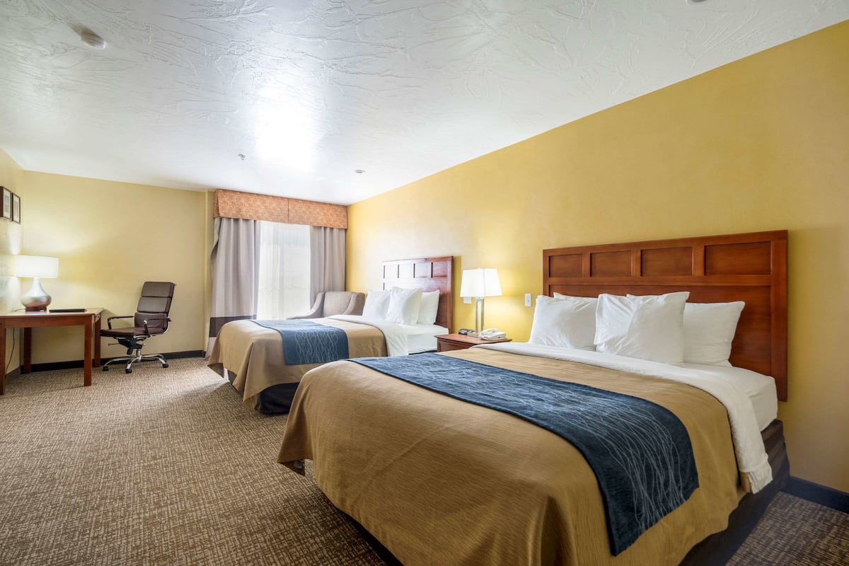 Habitación de hotel con dos camas, un escritorio, una silla y una ventana con cortinas.