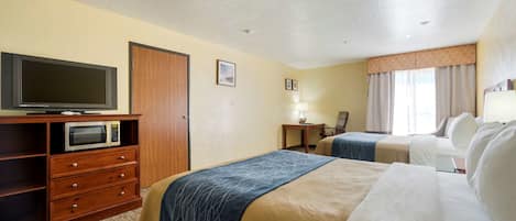 A hotel room with two beds, a TV, a microwave, a desk, and a lamp.