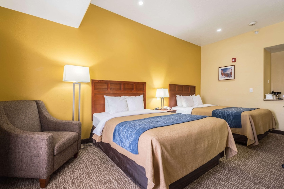 A hotel room with two beds, a sofa, and a lamp.