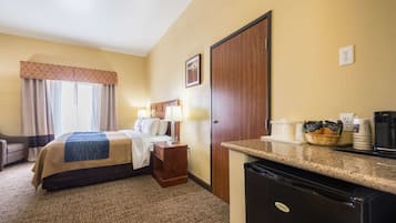 Camera d'albergo con un letto, comodino con lampada, scrivania con macchina del caffè e frigorifero.