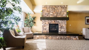 A living room with a stone fireplace, beige sofas, and a large potted plant. - Comfort Inn & Suites Cedar City South (Cedar City)