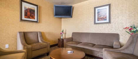 A living room with a brown sofa, two armchairs, a coffee table, and a flat-screen TV mounted on the wall.