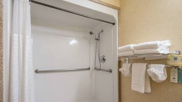 A shower area with a glass door, metal grab bars, and a towel rack with folded towels.