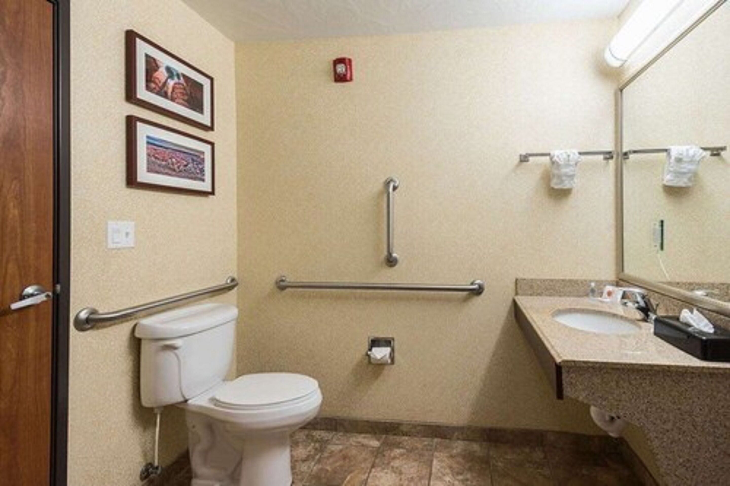 A standard hotel bathroom with a toilet, sink, and handrails.